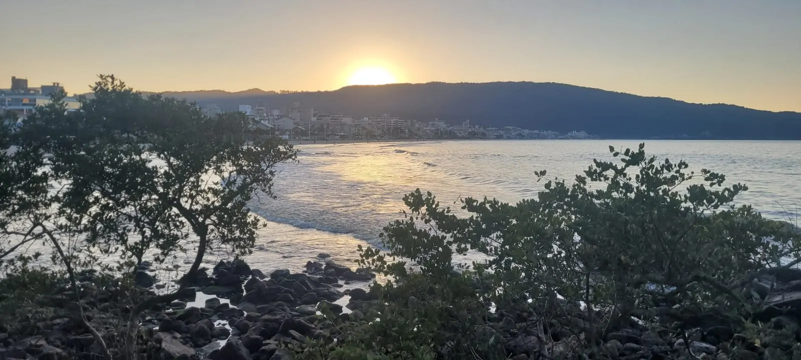Sol baixo sobre a baia, visto de uma costeira de pedras