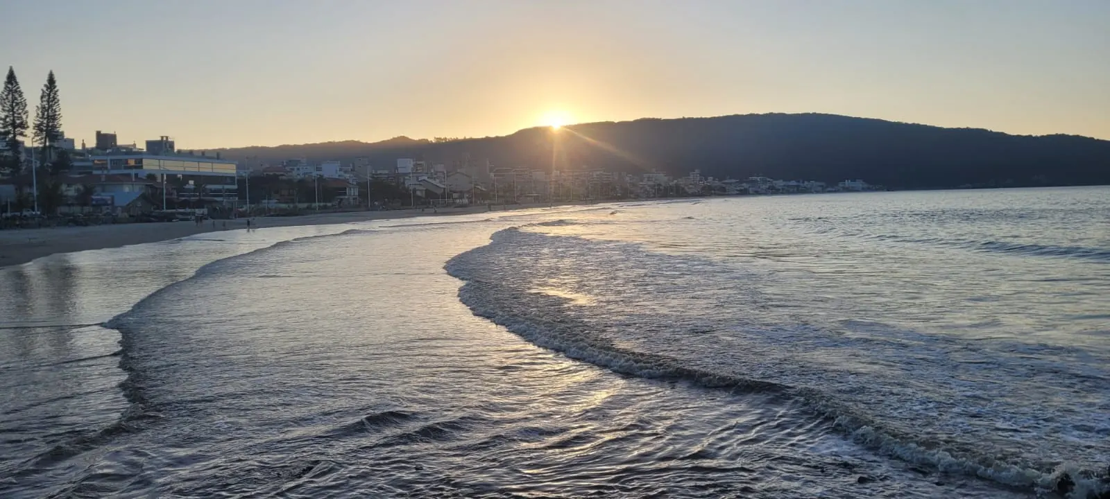 Fim de tarde numa praia do litoral, com a onda desenhando uma curva na areia